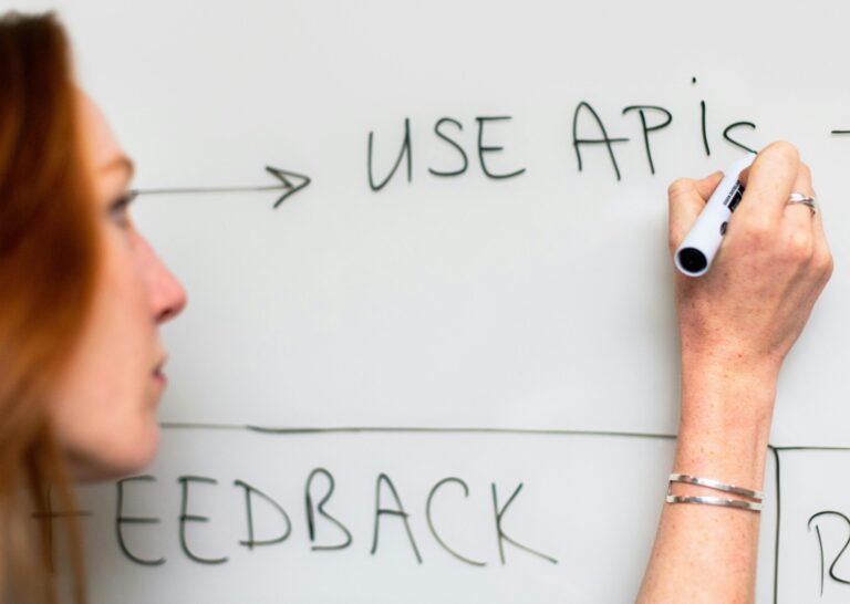 A woman writes 'Use APIs' on a whiteboard, focusing on software planning and strategy.